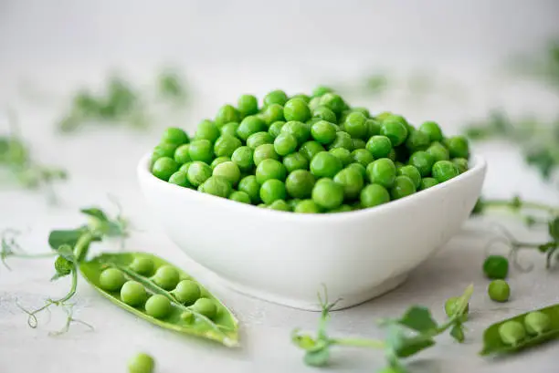 fresh green peas with greens and pea pods on a white plate