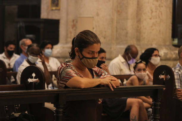 A cuban woman prays Havana - CUB; November 15, 2020: A woman prays during the celebration of a mass in the Cathedral of Havana and wears a face mask to protect herself from the coronavirus. nun praying cross human hand stock pictures, royalty-free photos & images