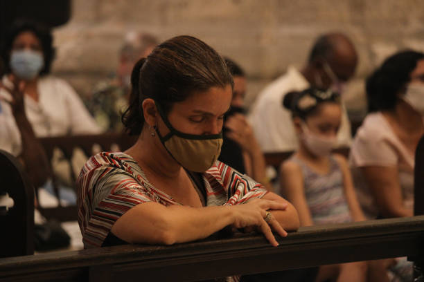 A cuban woman prays Havana - CUB; November 15, 2020: A woman prays during the celebration of a mass in the Cathedral of Havana and wears a face mask to protect herself from the coronavirus. nun praying cross human hand stock pictures, royalty-free photos & images