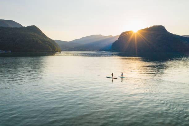 prospettiva aerea di due paddle boarder su un lago al tramonto - paddleboard oar women lake foto e immagini stock
