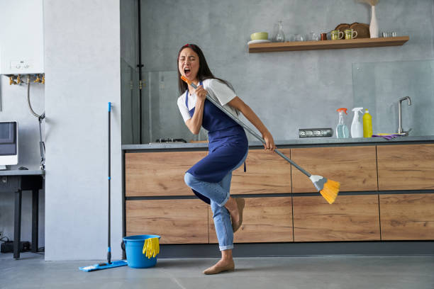 Happy worker. Full length shot of cheerful young woman, cleaning lady pretending to sing a song, holding broom while cleaning the floor, doing household chores Full length shot of cheerful young woman, cleaning lady pretending to sing a song, holding broom while cleaning the floor, doing household chores. Housework and housekeeping concept broom photos stock pictures, royalty-free photos & images