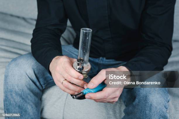 The Young Person Smoking Medical Marijuana With Bong Indoors Stock Photo - Download Image Now