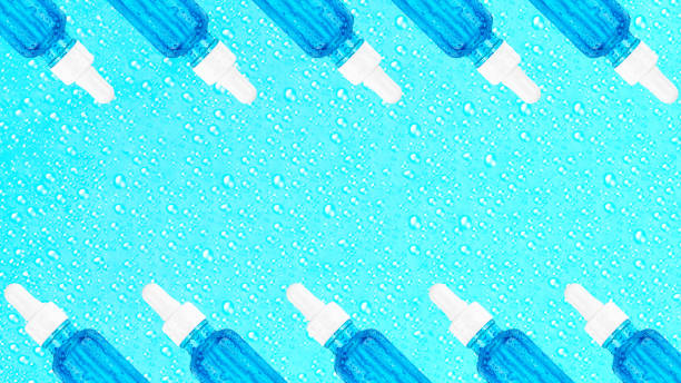 istock Moisturizing serum in glass bottle with white pipette on blue background with drops. Hyaluronic acid for hydration. Cosmetics pattern. Products for makeup and skin care. Banner. Place text. Copy space 1286013287