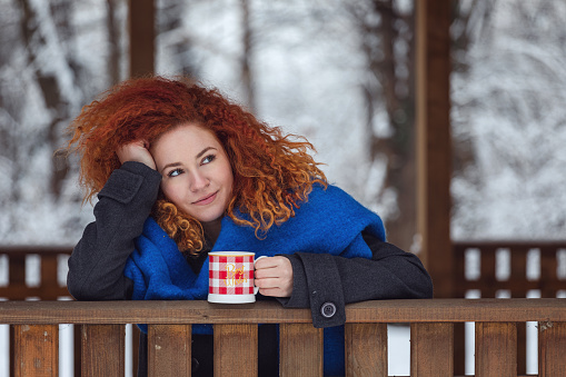 Young beautiful woman in warm clothing with cup of hot tea or coffee enjoying outdoors in the winter forest