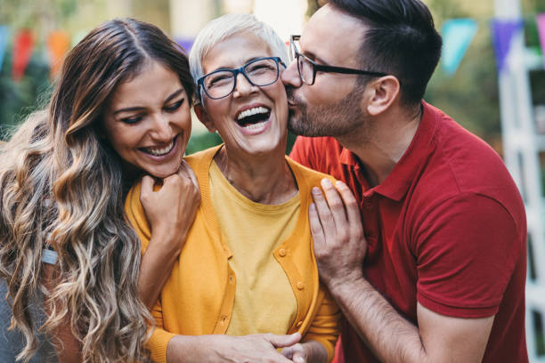 Adult son kissing his mother no the cheek Portrait of happy mother-in-law and a young couple in the back yard hand on shoulder photos stock pictures, royalty-free photos & images