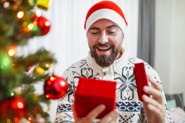 istock Smiling young man opening Christmas gift at home 1286015977