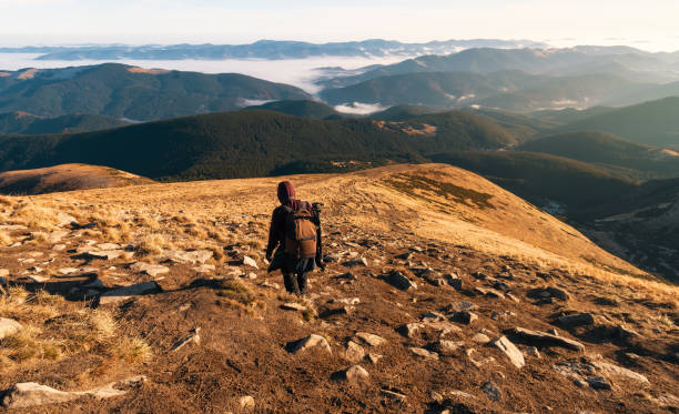 istock Lonely hiker with a backpack descends from the mountain peak along a path with stones against foggy mountains background. 1286016813