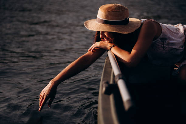 밀짚 모자를 쓴 로맨틱한 소녀가 보트에 앉아 손으로 물을 만진다. - yacht florida yachting nautical vessel 뉴스 사진 이미지