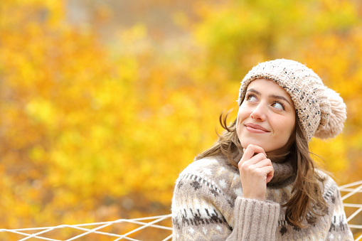 Pensive woman looks at side on a hammock in autumn