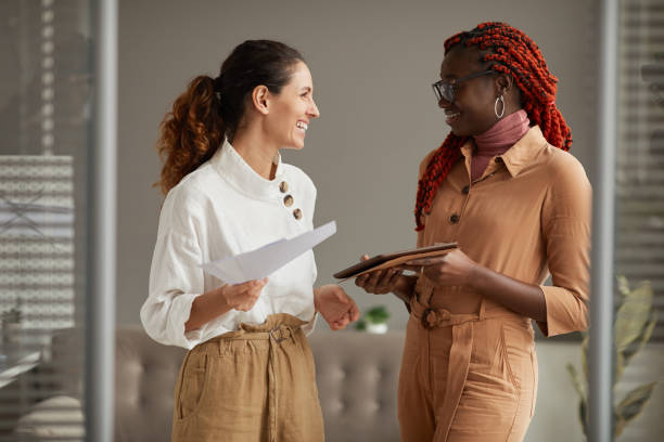 istock Two Smiling Young Women Chatting in Office 1286023688