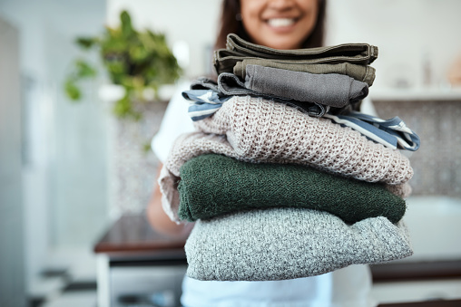 Closeup shot of a young woman holding a pile of folded laundry at home