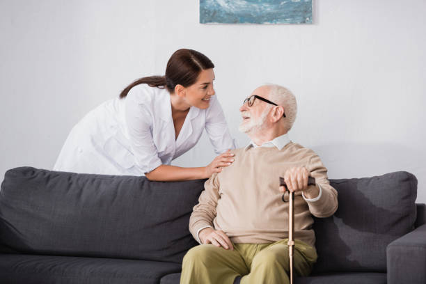 istock smiling geriatric nurse talking to elderly man sitting on sofa at home 1286024763