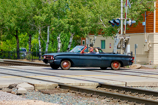 Flagstaff, Arizona / USA - July 25, 2020: A man drives his antique “Batman” car across the railroad tracks in the heart of the historic district in this Northern Arizona city.