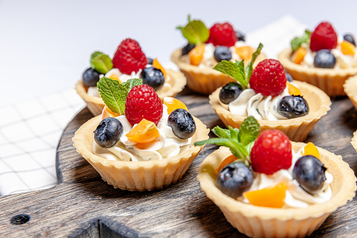 Fruit and berry tartlets dessert assorted on wooden tray. Closeup of delicious pastry sweets pies colorful cakes with fresh natural raspberry blueberry and cheese cream. French bakery catering