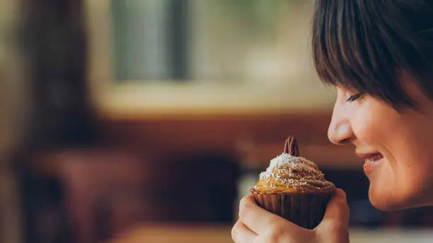 Cropped side portrait of a young woman smelling a tasty cupcake at a coffee house