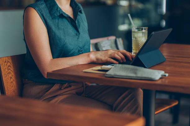 istock Telecommuting: Anonymous Young Businesswoman Working Remotely on her Tablet PC from a Cozy Cafe 1286034616