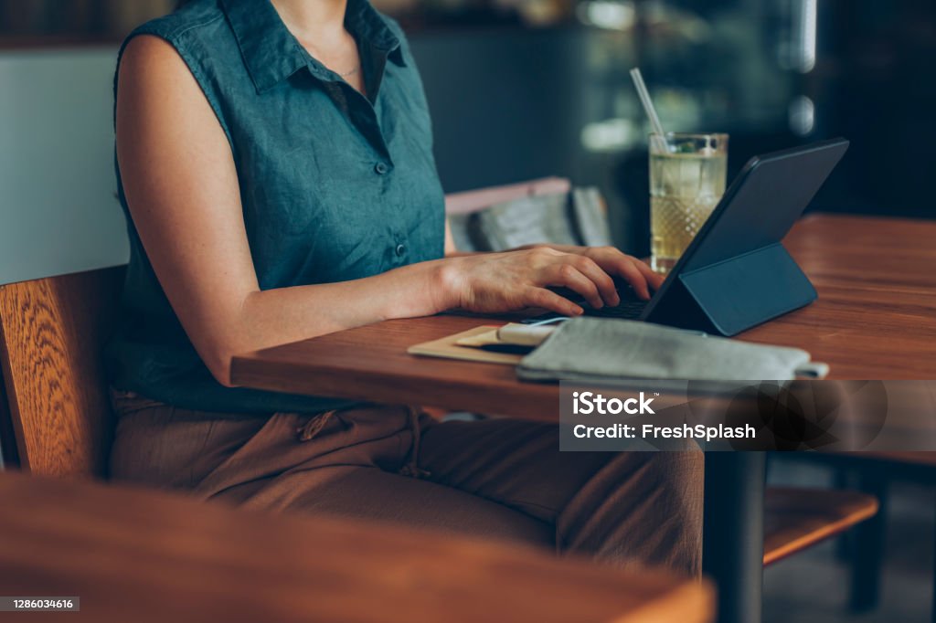 Telecommuting: Anonymous Young Businesswoman Working Remotely on her Tablet PC from a Cozy Cafe Unrecognizable female freelancer browsing the Internet on her tablet computer while having a glass of cold lemonade 30-34 Years Stock Photo