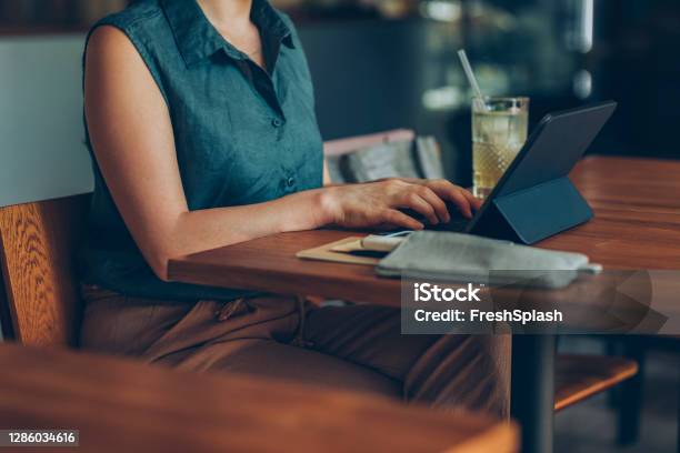 Telecommuting Anonymous Young Businesswoman Working Remotely On Her Tablet Pc From A Cozy Cafe Stock Photo - Download Image Now
