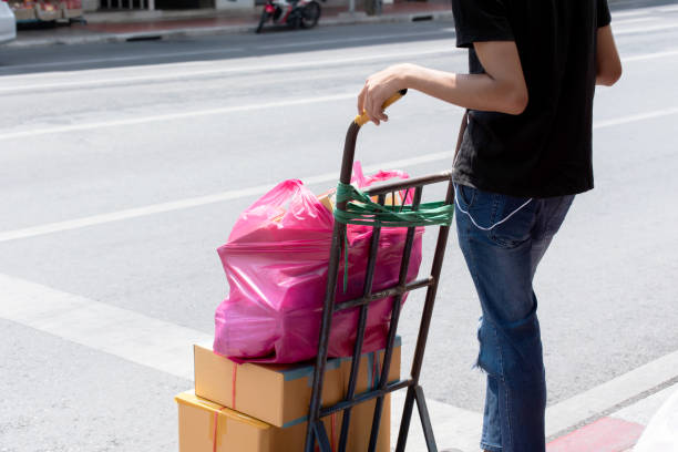 The delivery man is pushing two wheeled trolley to delivery goods in cardboard box. The delivery man is pushing two wheeled trolley to delivery goods in cardboard box.He waiting across the road in the sun for work. sack barrow stock pictures, royalty-free photos & images