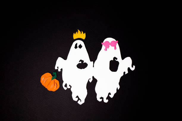 Two festive ghosts fly witch holiday pumpkin on a black background. The paper art photo was shot for your Halloween design.