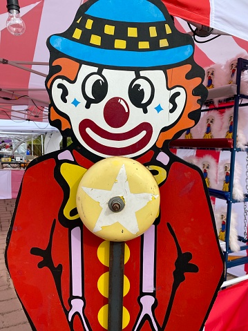 a creepy bald evil clown, in a gray costume with a white ruff around his neck, in front of a dirty and old circus tent, stares at the observer with a frightening smile