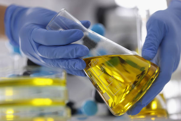 istock Hands in blue gloves hold flask with clear golden liquid in laboratory. 1286048718