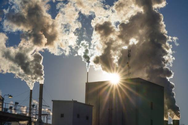 billowing smoke steam from factory plant with sun rays stock photo