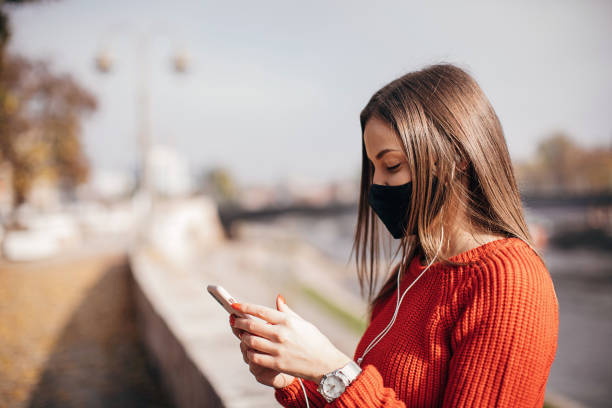 istock Woman with protective face mask using smart phone on the street 1286055119