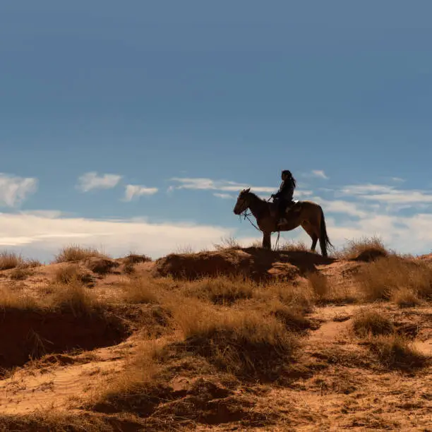 Photo of Navajo boy on horse silhouette against blue sky in Arizona