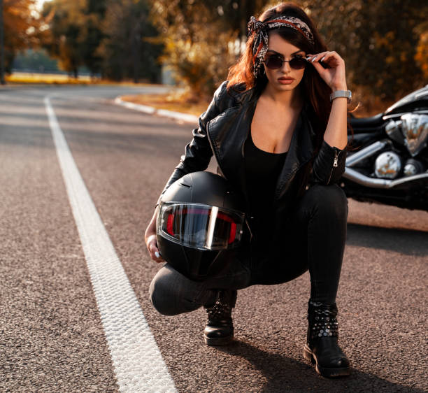 sexy chica caucásica arrodillada en la carretera junto a la motocicleta, usando gafas de sol y pañuelo - motorcycle women helmet sensuality fotografías e imágenes de stock