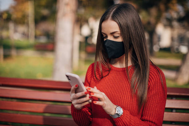 istock Woman with protective face mask using smart phone in park 1286055984