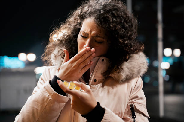 jeune femme dans la veste d’hiver toussant à l’extérieur et retenant la médecine - cough lozenge photos et images de collection