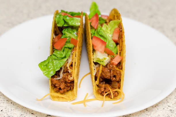 istock Two tacos on a white plate topped with lettuce, tomato, and cheese, ready to be served. 1286059149