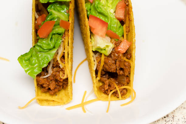 istock Two tacos on a white plate topped with lettuce, tomato, and cheese, ready to be served. 1286059155