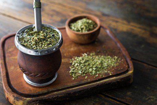 Traditional Argentinian yerba mate tea in a calabash gourd with bombilla stick against wooden background