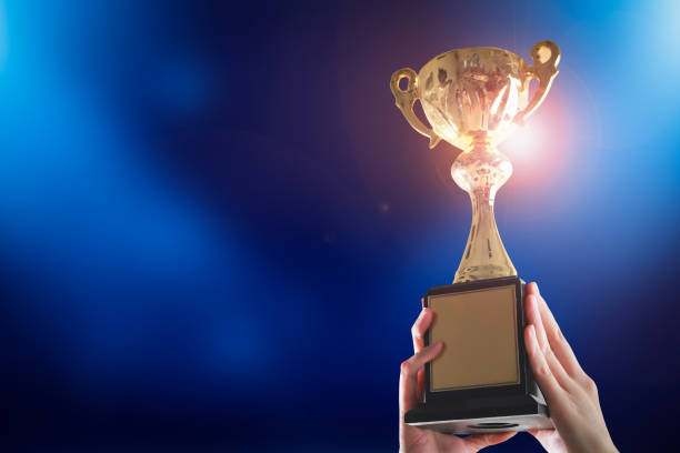 istock Business hands holding trophy cup on blue background. Selective focus 1286062797