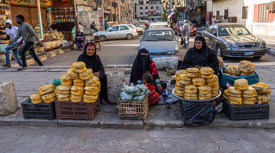 Egyptian women in traditional clothing selling baked goods at an Aswan souk, Egypt.
