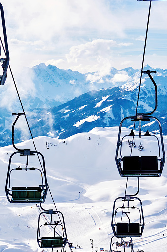 Ski lift with skiers above the slope of snowy Alpine mountains. Sports and recreational background
