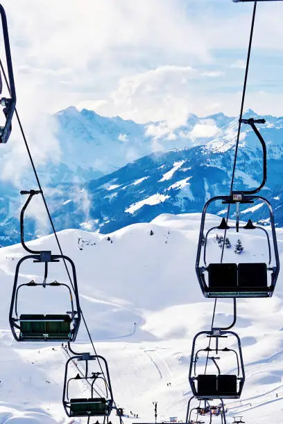 Photo of Ski lift with skiers above the slope of snowy Alpine mountains. Sports and recreational background