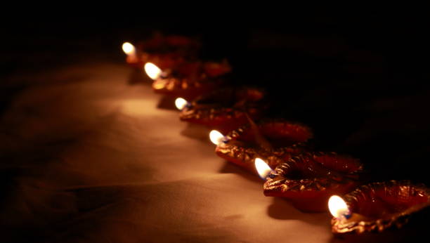 Indian traditional clay lamps with glowing flames kept together in a row during celebrations of indian hindu cultural festival of diwali or kali puja. photo taken with dark background and selective focus and shallow depth of field.concept depicting hope, good energy, peace. copy space background. close up shot. lámparas de arcilla tradicionales indias con llamas brillantes mantenidas juntas en una fila durante las celebraciones del festival cultural hindú indio de diwali o kali puja. foto tomada con fondo oscuro y enfoque selectivo y profundidad superficial de