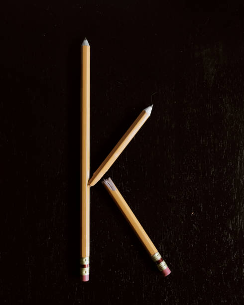 Lower case letter k made with broken pencils on sharp black background.