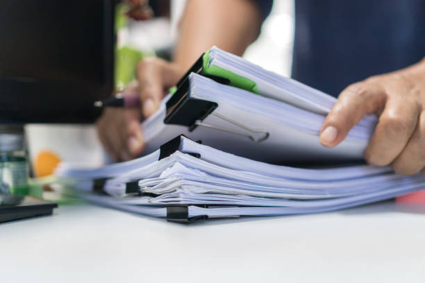 arquivos de papelada pesquisando conceito de negócio de informações, mãos de empresário digitando computador de teclado, trabalhando em pilhas de relatórios e pilhas de documentos inacabados alcança na mesa do escritório - stack of papers - fotografias e filmes do acervo