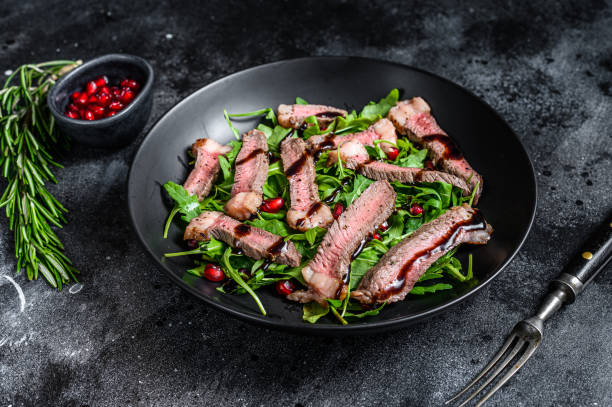 istock Grilled Beef Steak salad with arugula, pomegranate and greens vegetables. Black background. Top view 1286081868
