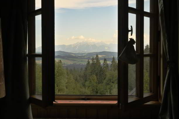 istock Beautiful view on green trees forest, blue sky and mountains through a wooden window frame of an old house cottage on a slope of a hill in southern Poland 1286087125