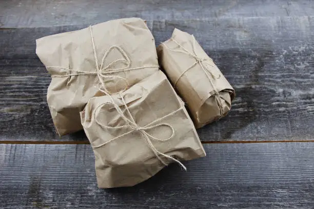 Gifts goods wrapped in craft paper and tied with a scourge on rough woodboard background. Eco-friendly packaging. Zero waste