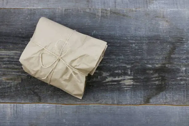 Gifts goods wrapped in craft paper and tied with a scourge on rough woodboard background. Eco-friendly packaging. Zero waste. Copy space.