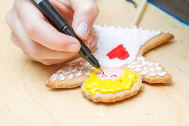 Children's master class of decorating ginger cakes with colored glaze. Girl paints the ginger cookie. Christmas Treats. Handmade cookies. Closeup, selective focus