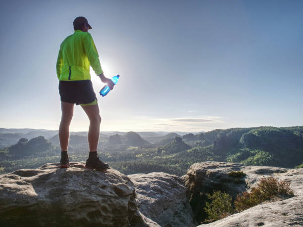 istock Runner In Yellow Green Shinning Jacket And Black Shorts Jumping On Rock. Man Athlete While Jumping 1286089633