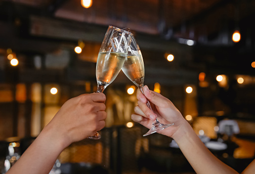 Cropped shot of unrecognizable Asian couple holding and toasting champagne flutes in a restaurant