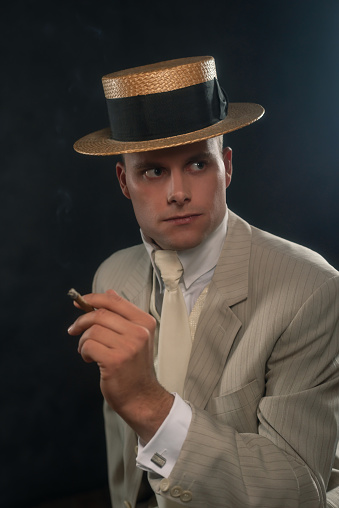 Man wearing boater hat and suit smoking cigar.